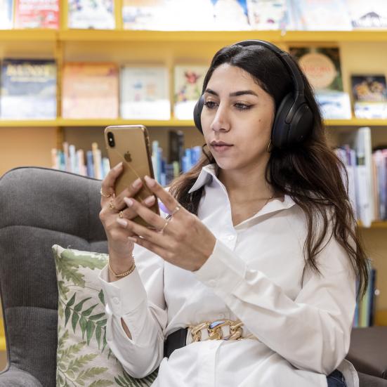 Kvinde sidder med sin telefon og har høretelefoner på 