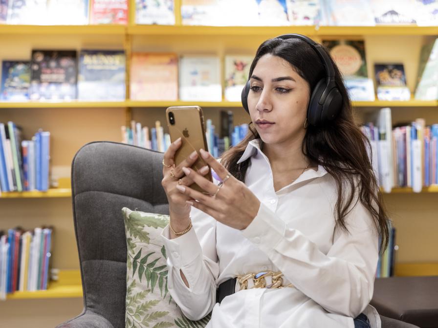 Kvinde sidder med sin telefon og har høretelefoner på 