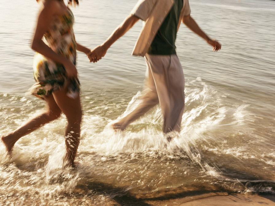 Et par på stranden holder hinanden i hånden mens de løber langs vandkanten.