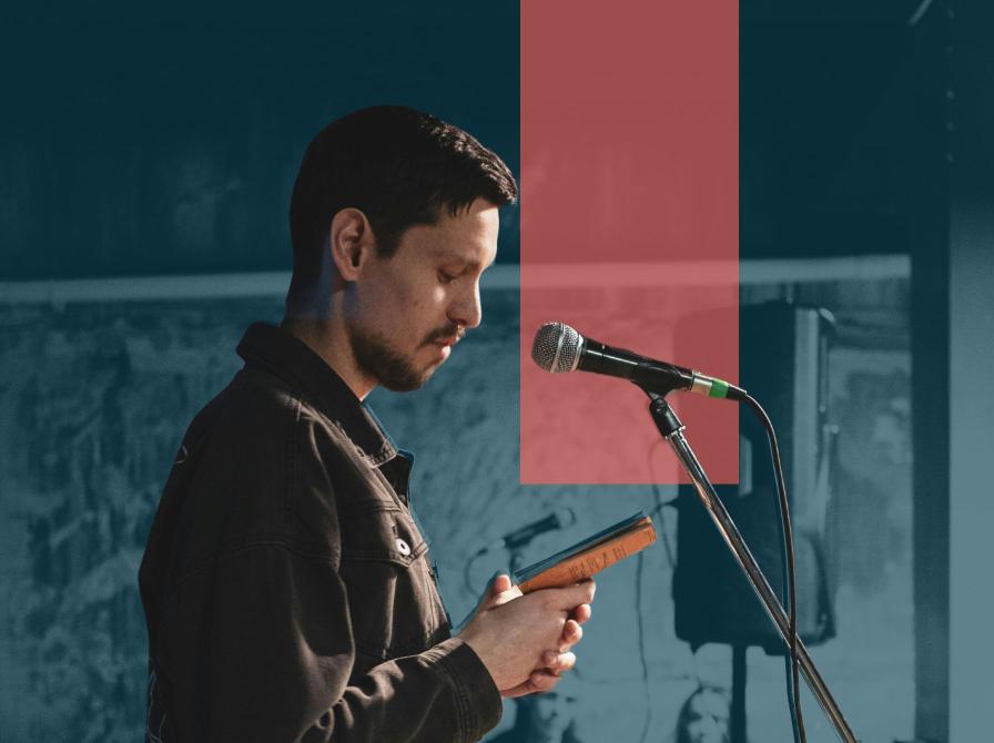 Mand læser op ved mikrofon og står med bog i hånden